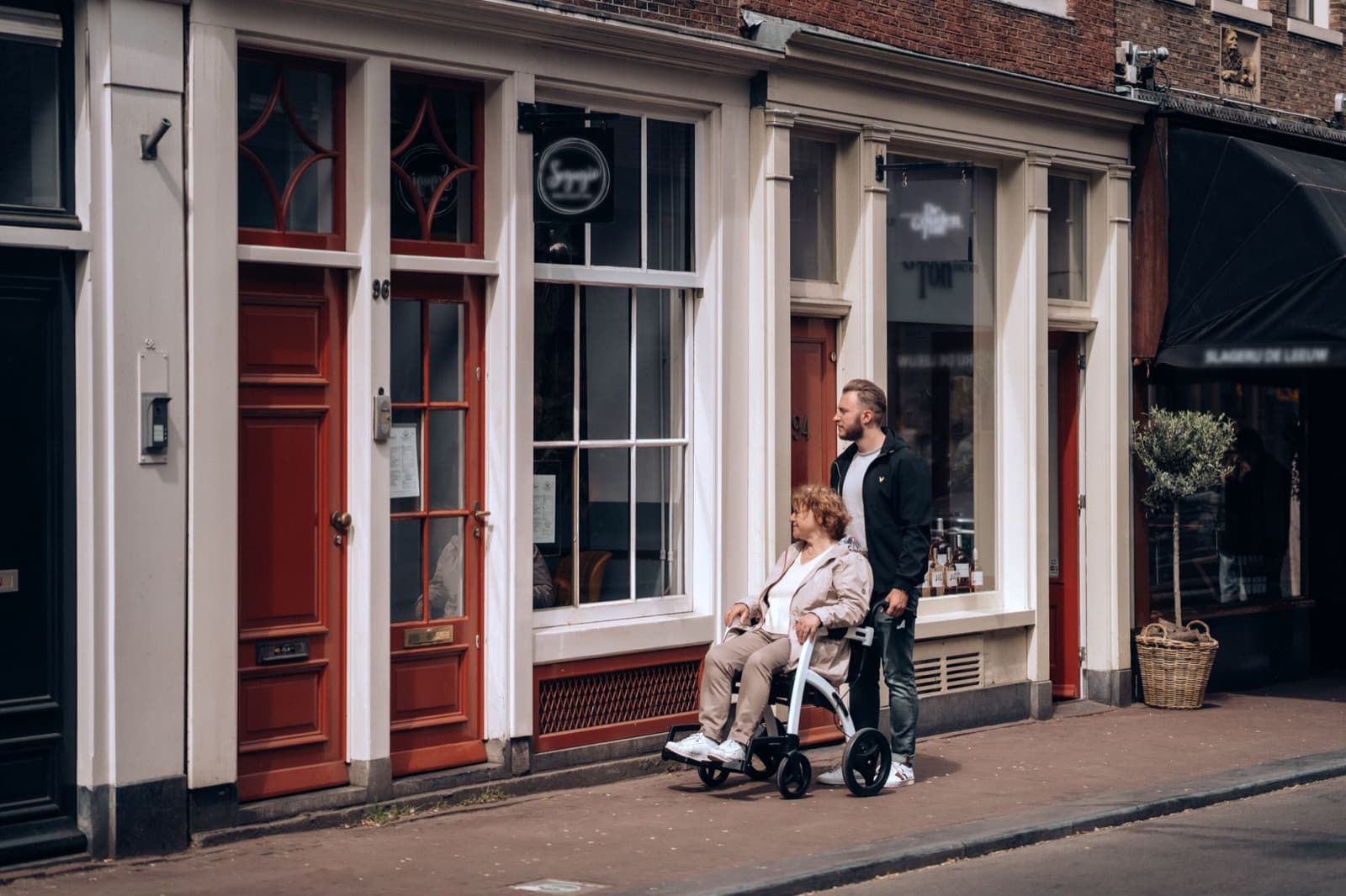 Een man duwt een vrouw in een rolstoel door een Nederlandse straat met bakstenen huizen