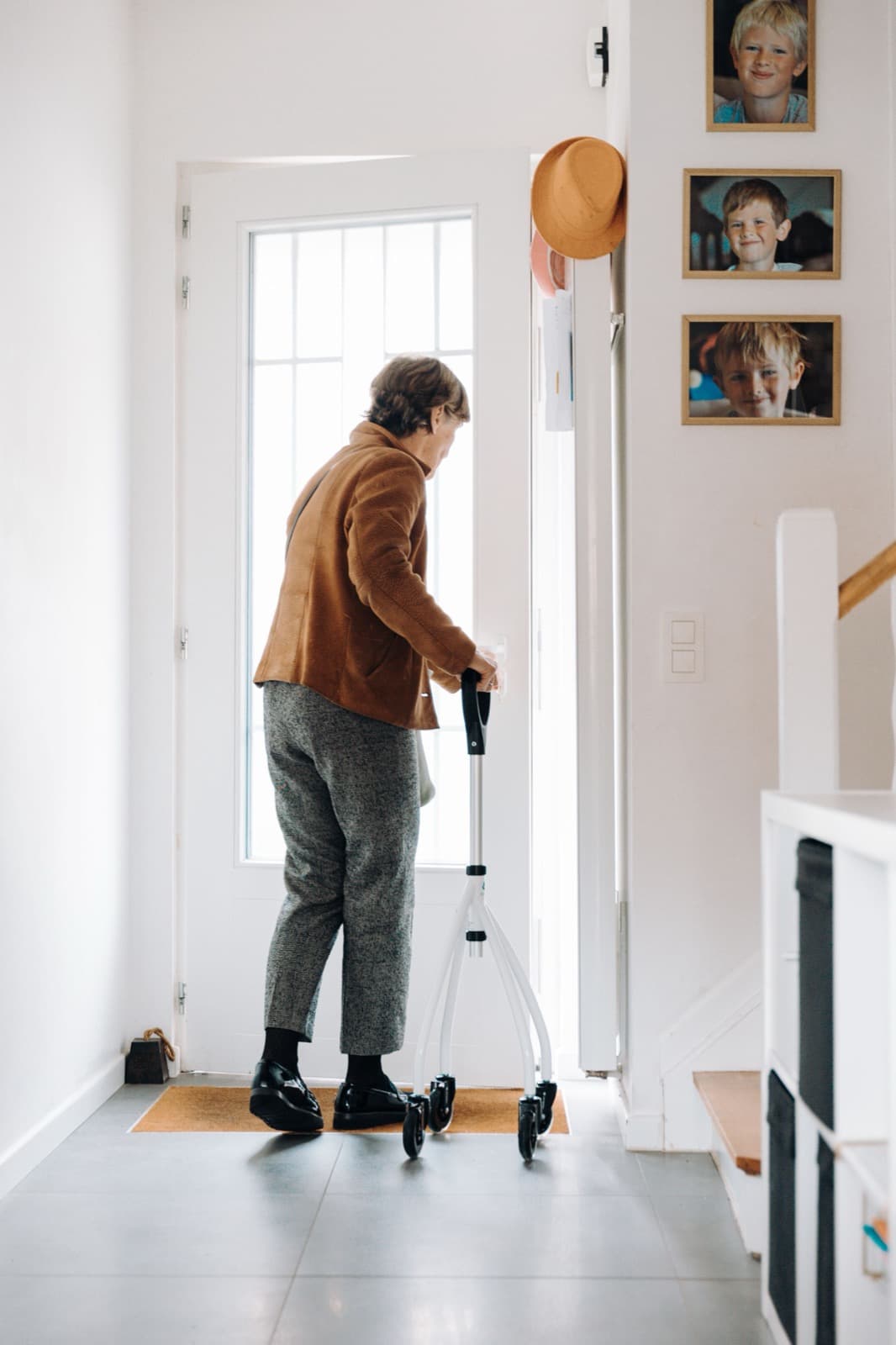 Een oudere vrouw loopt met een rollator naar de voordeur van haar huis