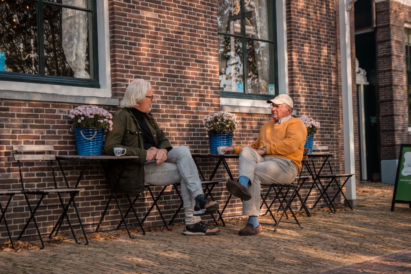 Twee ouderen drinken koffie en praten op een terras in de buurt