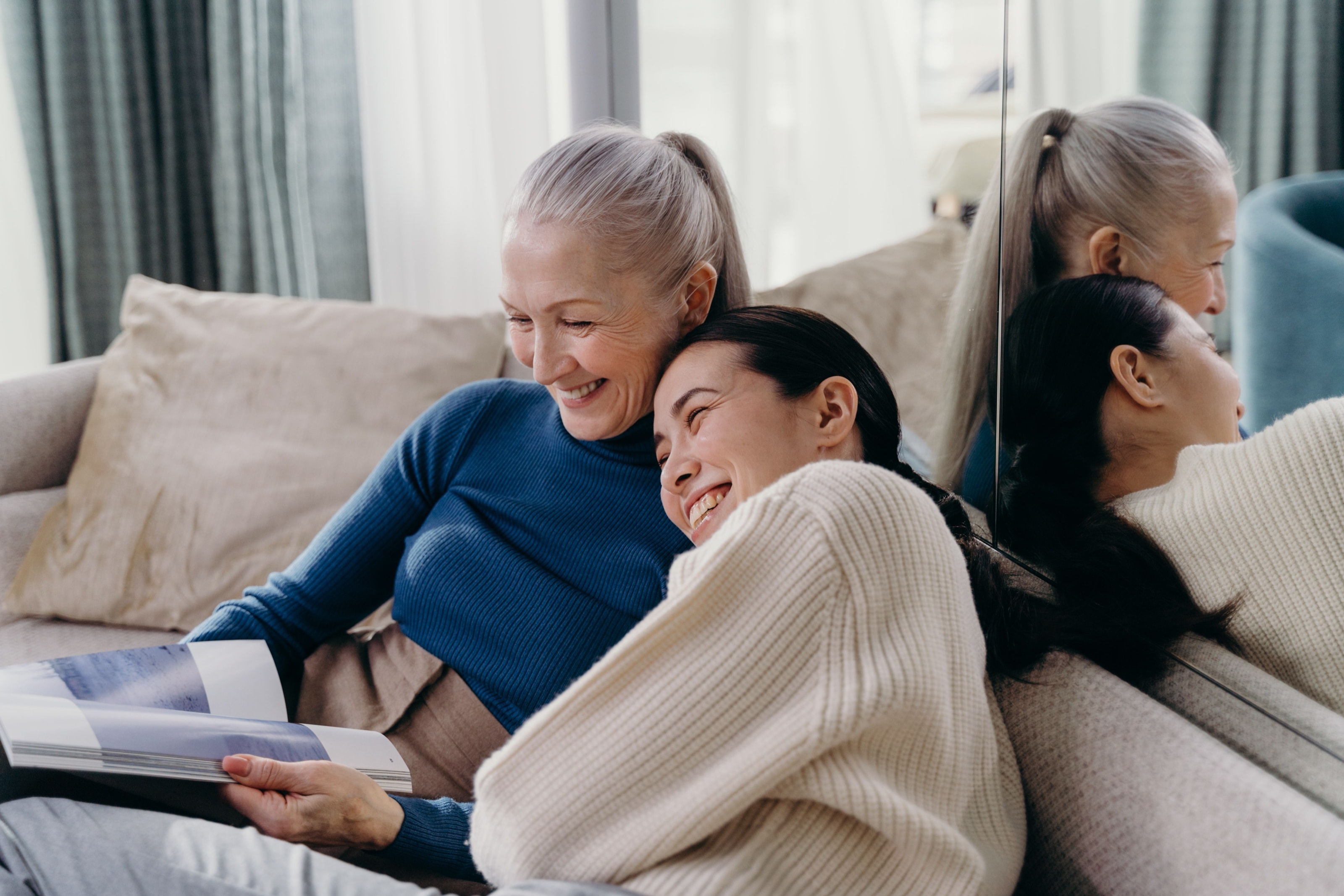 Een jonge en een oudere vrouw lachen samen op de bank